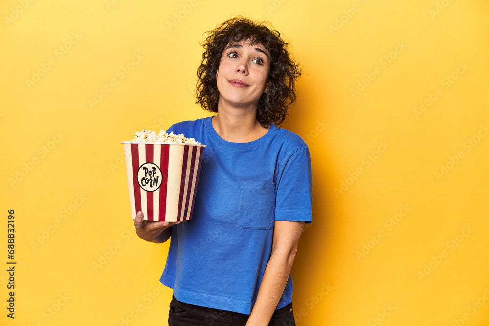 Curly-haired woman with popcorn for movie, studio dreaming of achieving goals and purposes Curly-haired woman with popcorn for movie, studio dreaming of achieving goals and purposes
