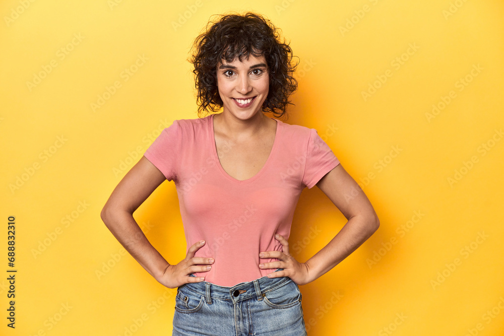 Curly-haired Caucasian woman in pink t-shirt confident keeping hands on hips. Curly-haired Caucasian woman in pink t-shirt confident keeping hands on hips.
