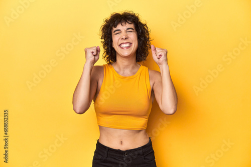 Curly-haired Caucasian woman in yellow top celebrating a victory, passion and enthusiasm, happy expression.