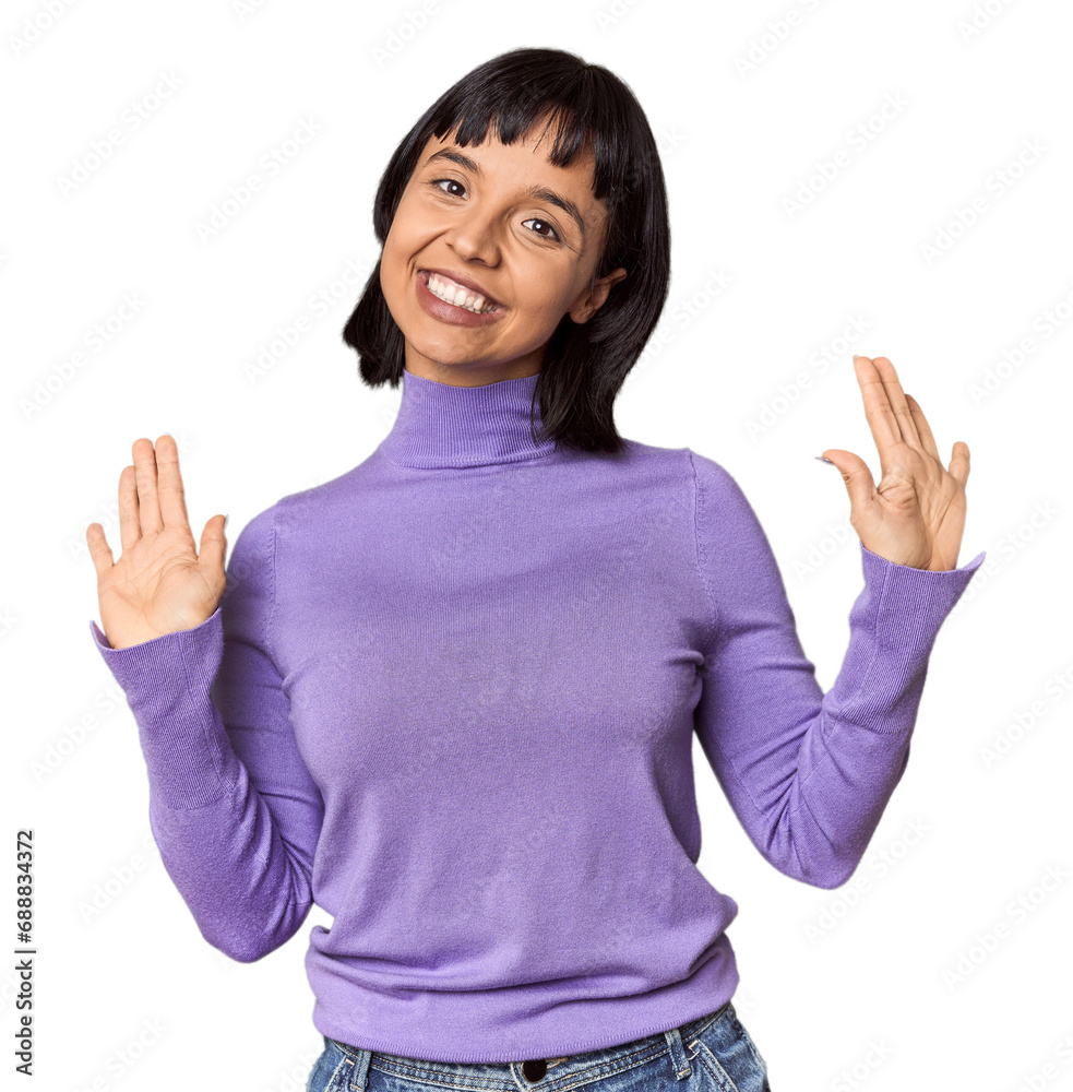 Young Hispanic woman with short black hair in studio receiving a pleasant surprise, excited and raising hands.