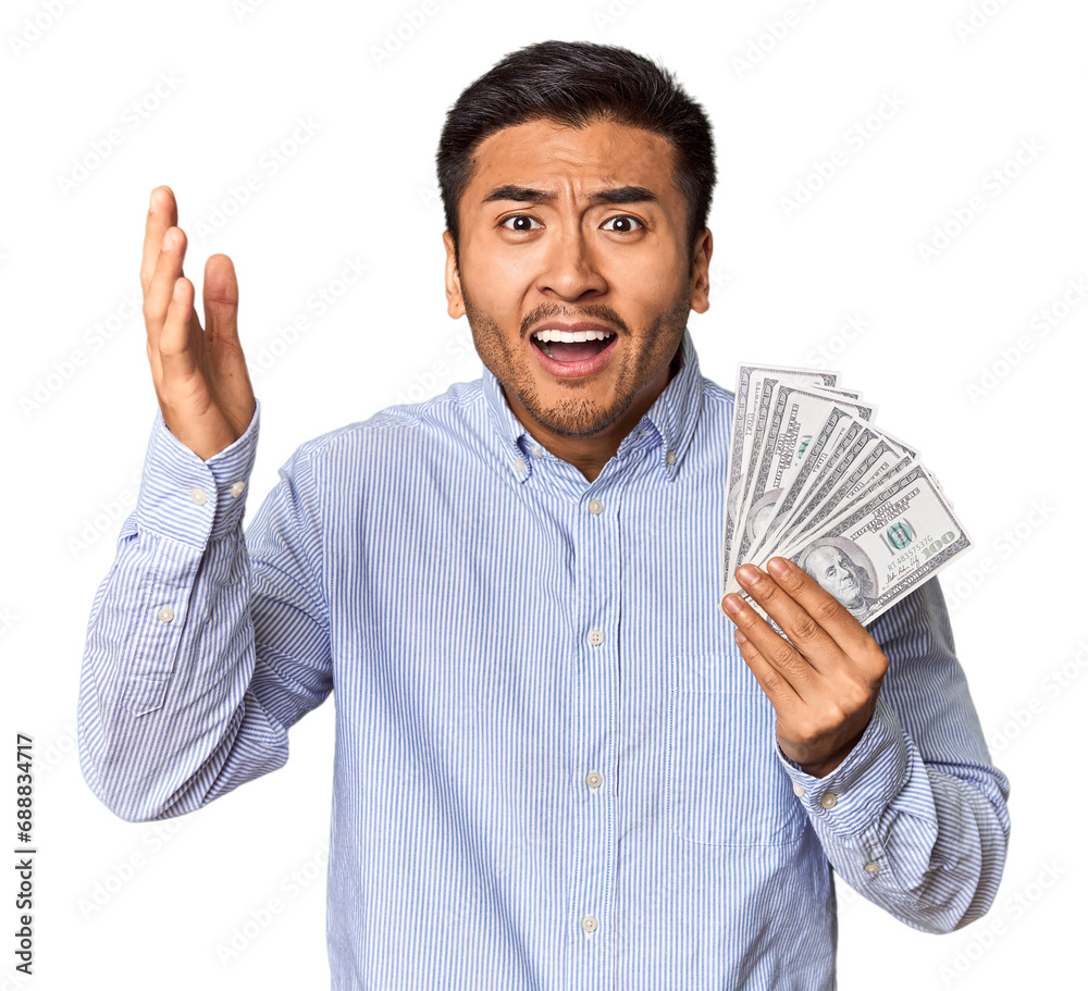 Young Chinese man holding dollar bills in studio receiving a pleasant surprise, excited and raising hands. Young Chinese man holding dollar bills in studio receiving a pleasant surprise, excited and raising hands.