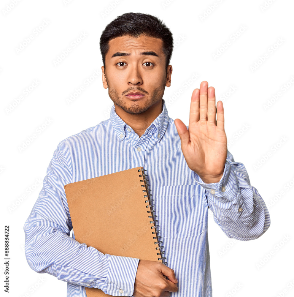 Chinese student with a notebook in studio standing with outstretched hand showing stop sign, preventing you. Chinese student with a notebook in studio standing with outstretched hand showing stop sign, preventing you.