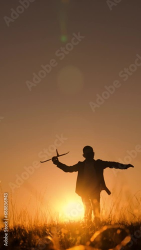 Child boy wants to become pilot astronaut, Airplane flight. Happy Child boy plays with toy plane on field, sunset. Children play with toy airplane. Teenager dreams of flying, becoming pilot. Childhood photo