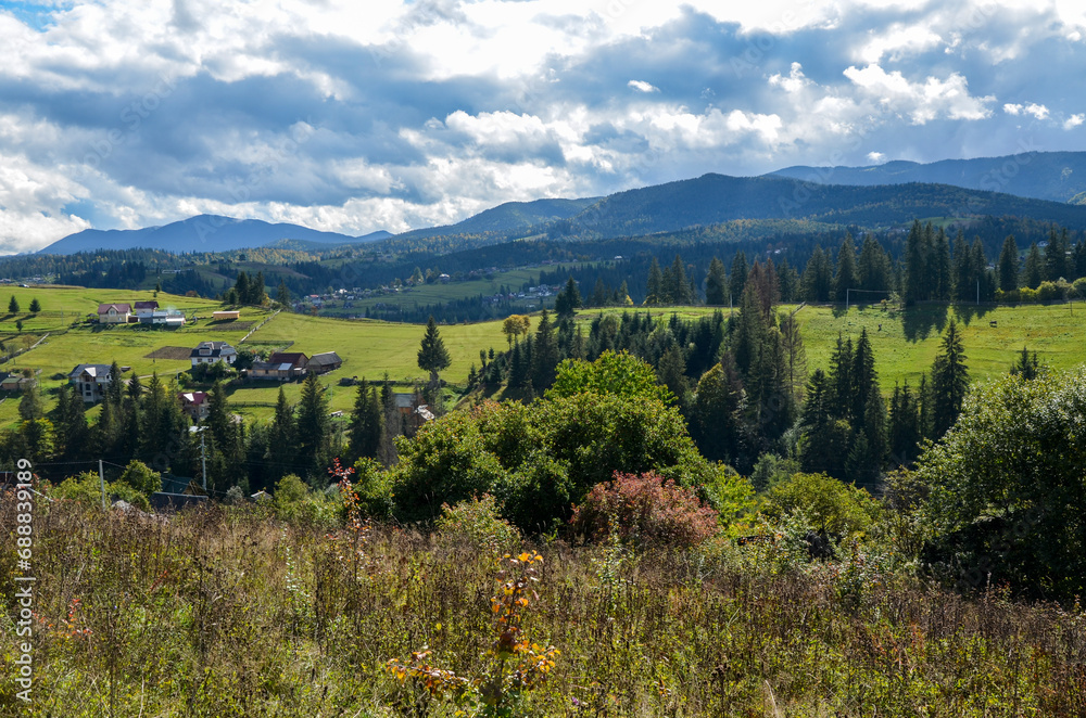 Beautiful landscape of Carpathian Mountains ridge with rolling grassy hills, forest and rural houses during a sunny summer day