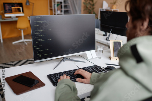 Over shoulder view at software developer writing code in office with focus on computer screen, copy space