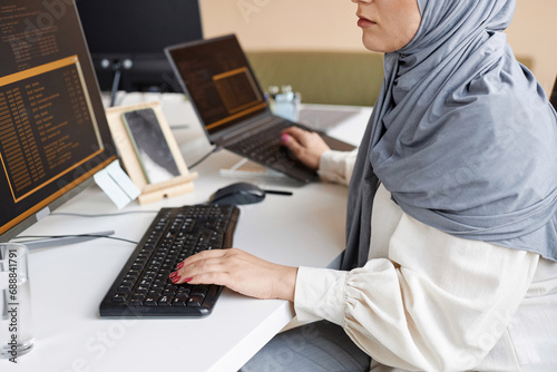 Closeup of Muslim young woman working as female software developer and writing code with multiple computer devices, copy space