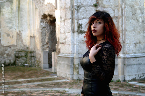 Amidst ruins, a red-haired dark beauty, half-bust framed, explores the mystery of an abandoned abbey with a haunting allure.