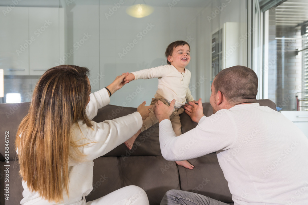 Fototapeta premium Happy family playing and lifting a baby in the sofa