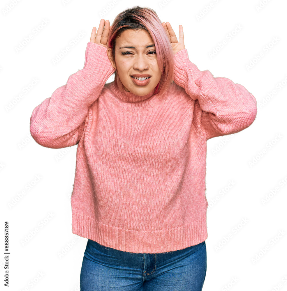 Hispanic woman with pink hair wearing casual winter sweater trying to hear both hands on ear gesture, curious for gossip. hearing problem, deaf