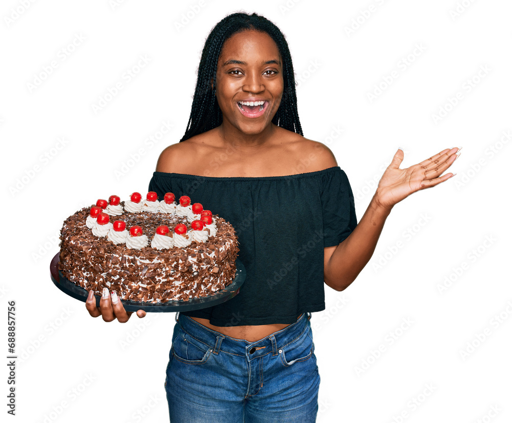 Young african american woman celebrating birthday holding big chocolate cake celebrating victory with happy smile and winner expression with raised hands Young african american woman celebrating birthday holding big chocolate cake celebrating victory with happy smile and winner expression with raised hands
