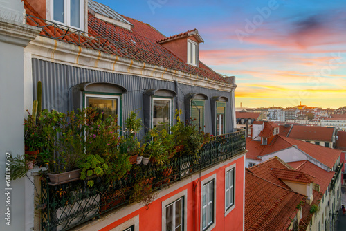 View from an alley with colorful residential buildings and terraces in the Alfama district overlooking the city of Lisbon Portugal at sunset. 