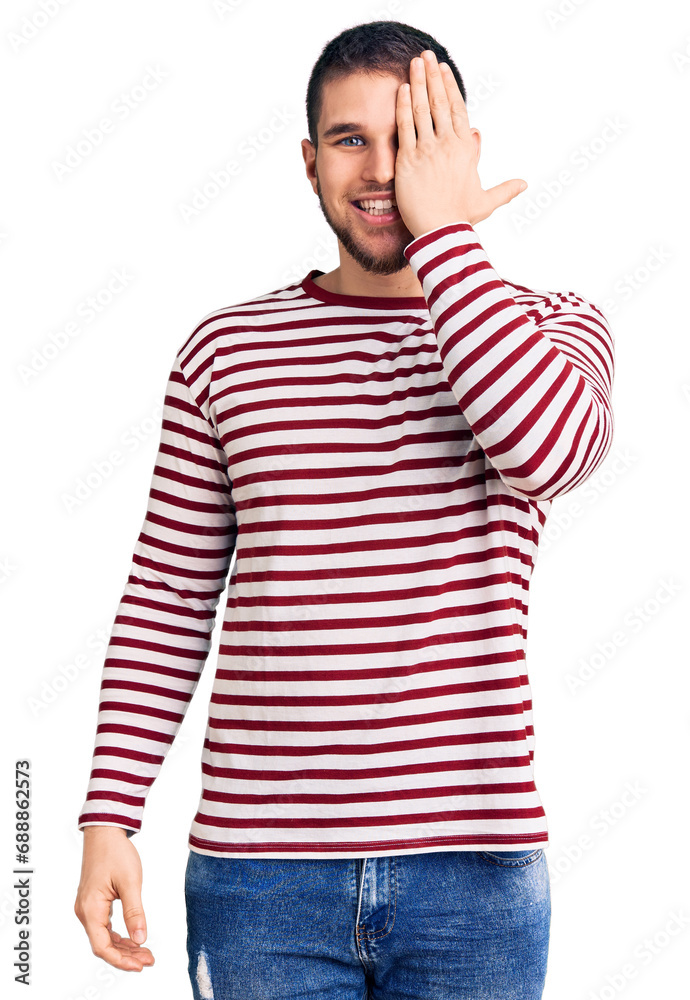 Young handsome man wearing striped sweater covering one eye with hand, confident smile on face and surprise emotion. Young handsome man wearing striped sweater covering one eye with hand, confident smile on face and surprise emotion.