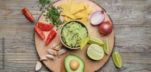 Tasty guacamole with fresh vegetables and nachos on wooden background