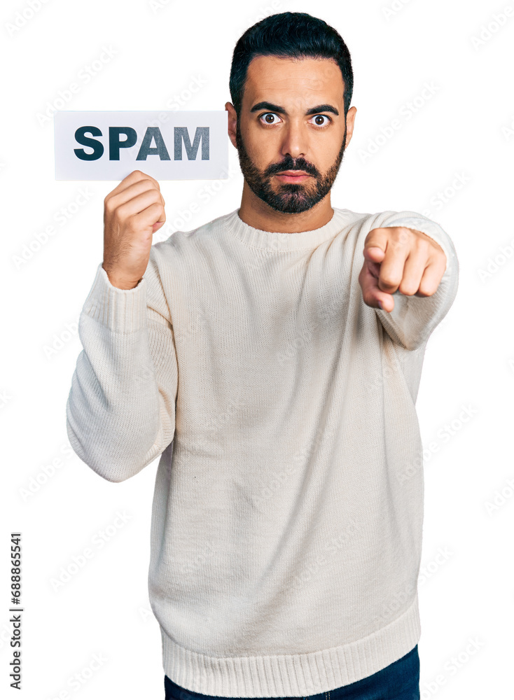 Young hispanic man with beard holding spam banner pointing with finger to the camera and to you, confident gesture looking serious Young hispanic man with beard holding spam banner pointing with finger to the camera and to you, confident gesture looking serious