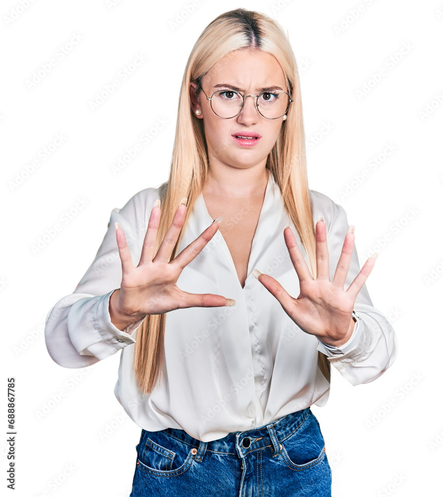 Beautiful blonde woman wearing elegant shirt and glasses afraid and terrified with fear expression stop gesture with hands, shouting in shock. panic concept. Beautiful blonde woman wearing elegant shirt and glasses afraid and terrified with fear expression stop gesture with hands, shouting in shock. panic concept.
