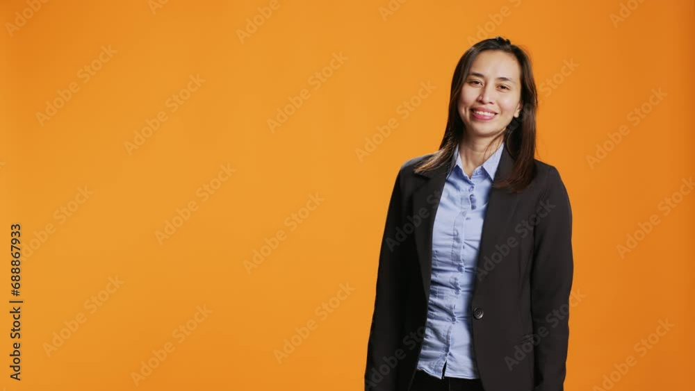 Businesswoman shows left and right directions in studio, creating new internet advertisement over orange background. Asian person working on marketing web commercial on camera.