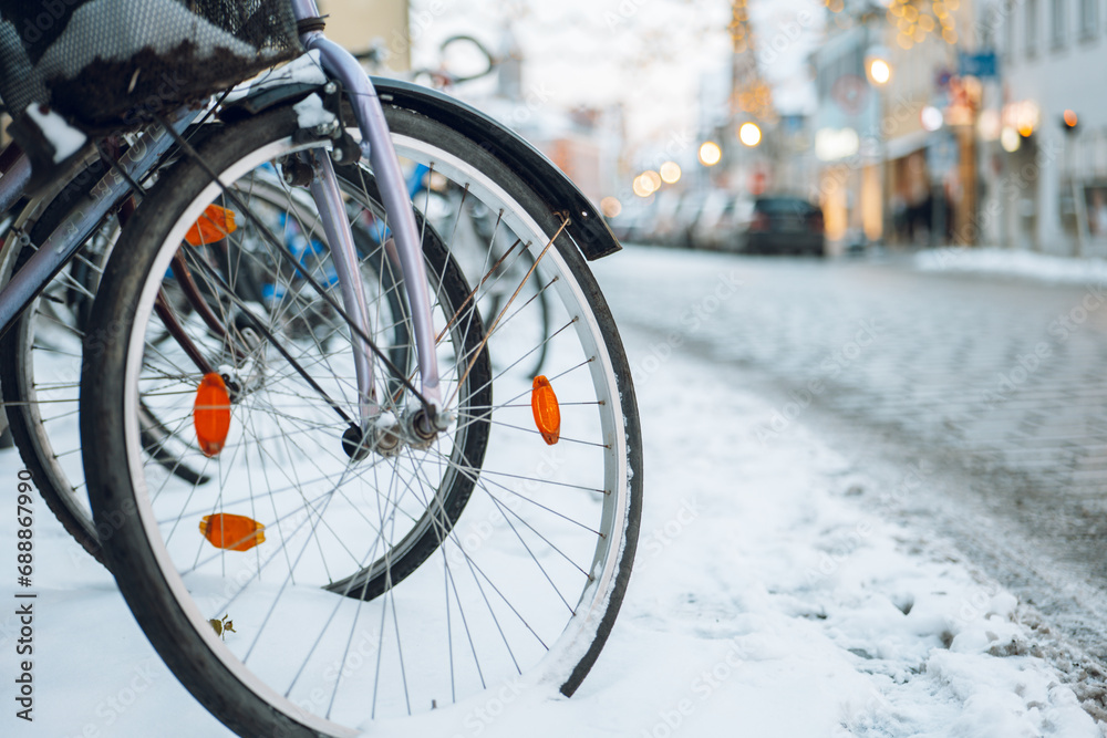 Winter in the city. Bicycle wheels in snow on blurred city background.Snowy winter weather