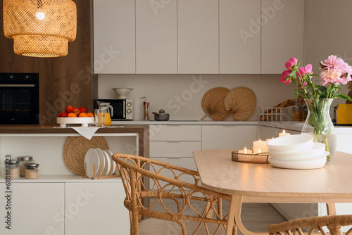 Dining table with peony flowers  burning candles and bowls in modern kitchen with glowing lamp