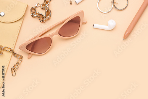 Composition with stylish sunglasses, modern earphones and female accessories on beige background