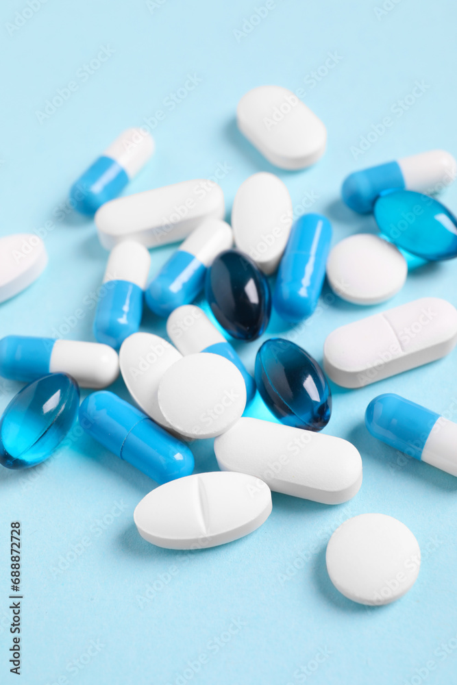 Many different pills on light blue background, closeup