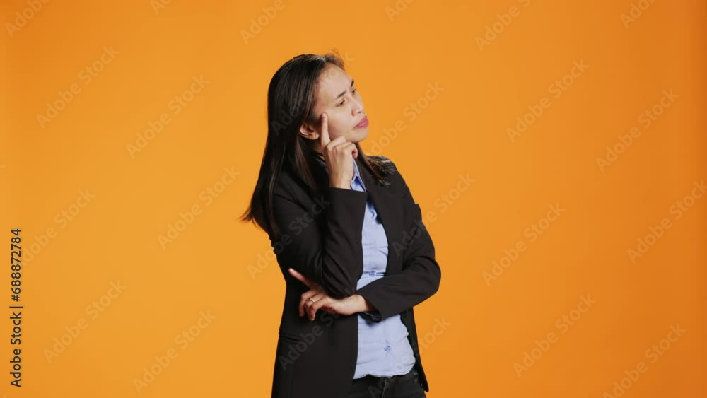 Thoughtful businesswoman posing over orange backdrop, thinking about new ideas and being in doubt. Clueless uncertain person brainstorming solutions, acting focused in front of camera.