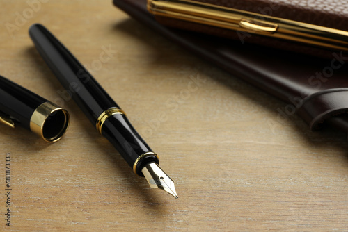 Stylish fountain pen, notebook and cigarette case on wooden table, closeup