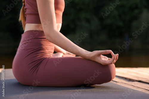 Woman practicing Padmasana on yoga mat on wooden pier outdoors, closeup. Lotus pose