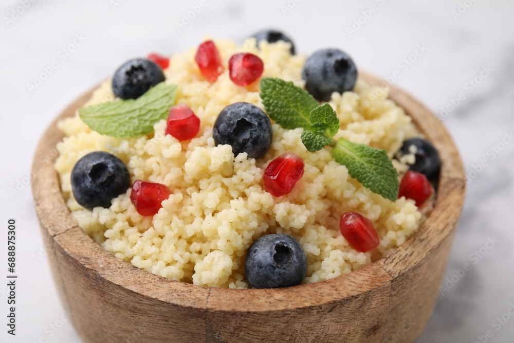 Bowl of tasty couscous with blueberries, pomegranate and mint on white table, closeup