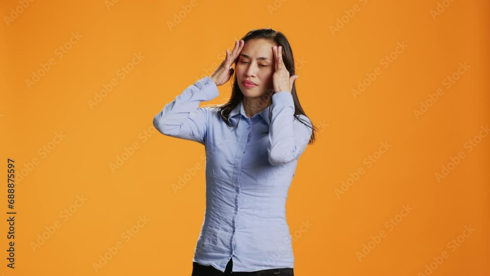 Asian young adult suffers from painful migraine in studio, rubbing temples to ease temples pressure. Sick worried woman feeling under stress, dealing with headache and tension. Asian young adult suffers from painful migraine in studio, rubbing temples to ease temples pressure. Sick worried woman feeling under stress, dealing with headache and tension.