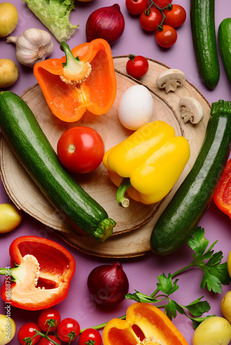 Wooden boards with fresh vegetables and greenery on purple background