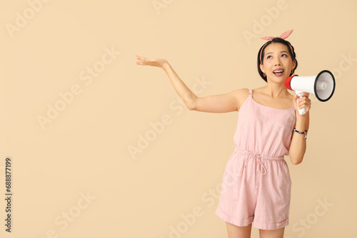 Young Asian woman with megaphone showing something on beige background