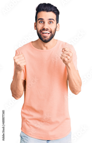 Young handsome man with beard wearing casual t-shirt celebrating surprised and amazed for success with arms raised and open eyes. winner concept.