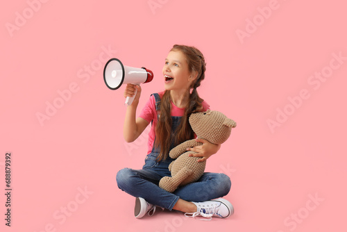 Little girl with megaphone and teddy bear sitting on pink background