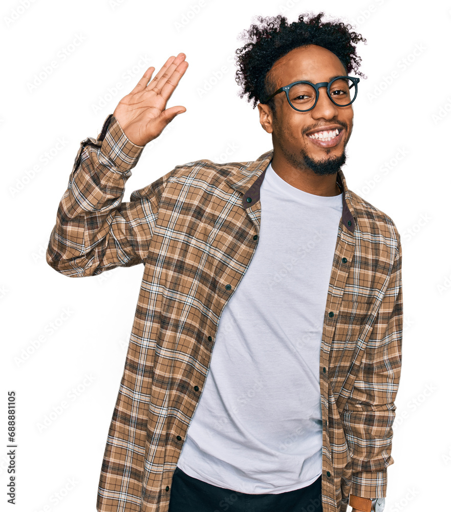 Naklejka premium Young african american man with beard wearing casual clothes and glasses waiving saying hello happy and smiling, friendly welcome gesture
