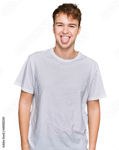 Young caucasian man wearing casual white t shirt sticking tongue out happy with funny expression. emotion concept.