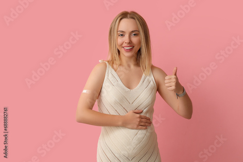 Young pregnant woman after vaccination showing thumb-up on pink background