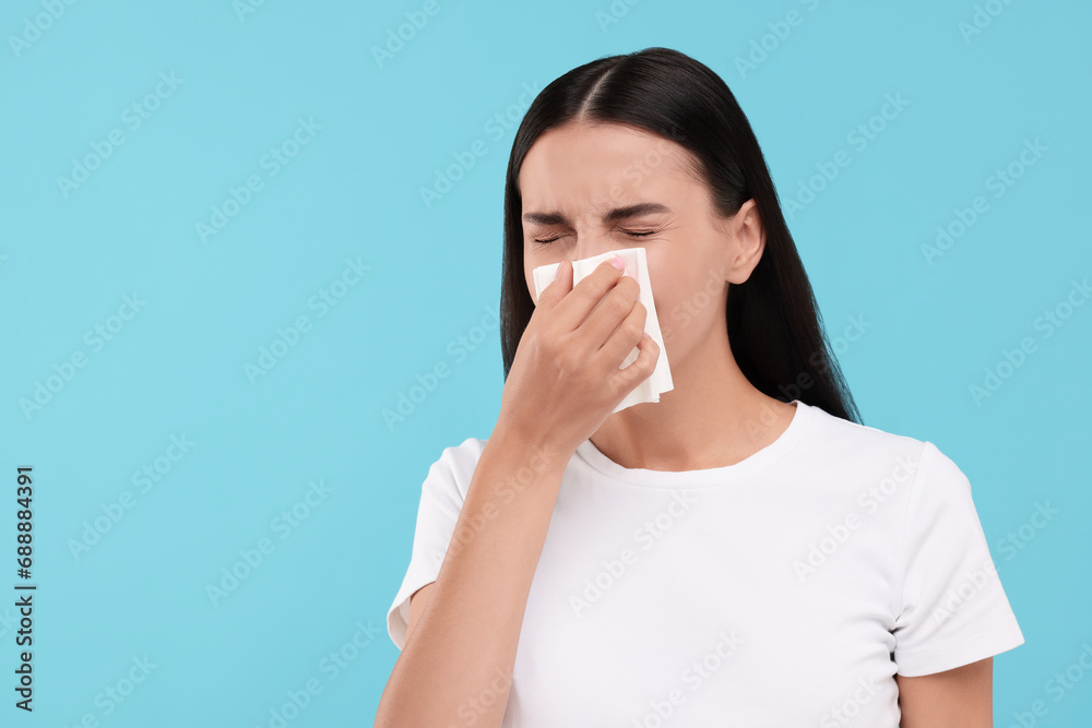 Suffering from allergy. Young woman blowing her nose in tissue on light blue background. Space for text Suffering from allergy. Young woman blowing her nose in tissue on light blue background. Space for text