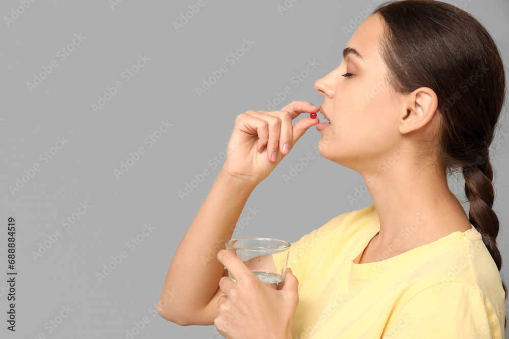 Pretty young woman taking vitamin A capsule on grey background Pretty young woman taking vitamin A capsule on grey background