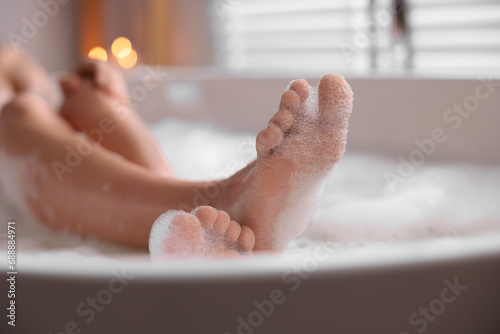 Woman taking bath in tub with foam indoors, closeup photo