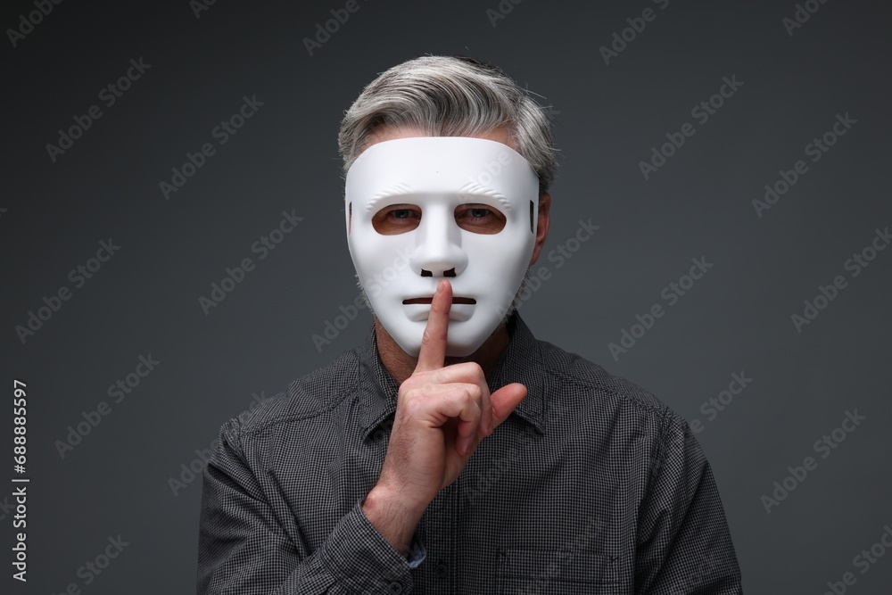 Man in mask showing hush gesture against dark grey background Man in mask showing hush gesture against dark grey background