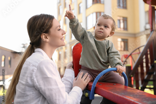Happy nanny and cute little boy on seesaw outdoors photo