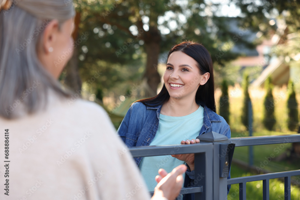 Friendly relationship with neighbours. Happy women near fence outdoors Friendly relationship with neighbours. Happy women near fence outdoors