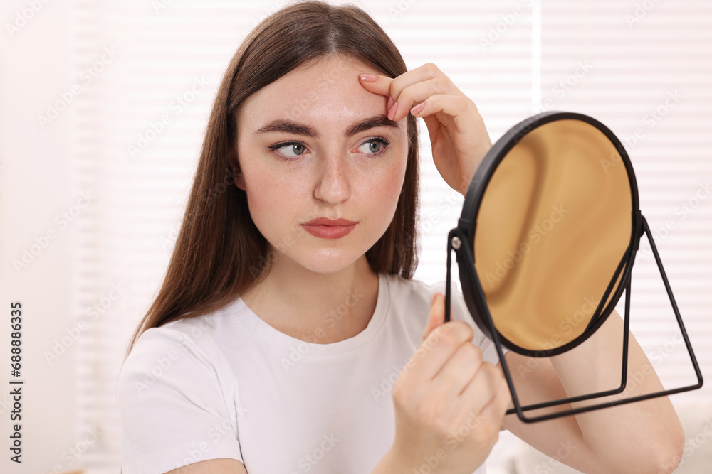 Young woman with skin problem looking at mirror indoors Young woman with skin problem looking at mirror indoors