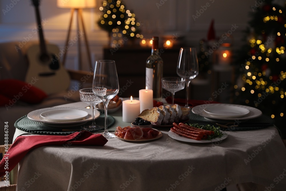 Christmas table setting with burning candles, appetizers and dishware in room