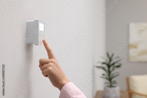 Woman adjusting thermostat on white wall indoors, closeup and space for text. Smart home system