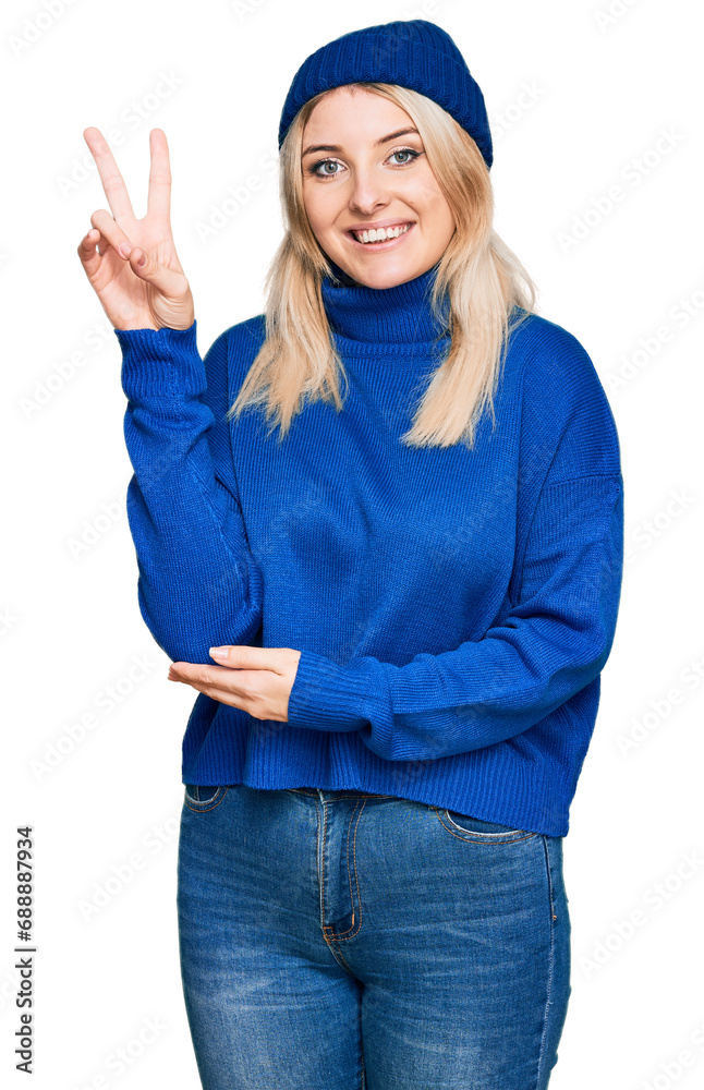 Φωτογραφία Young caucasian woman wearing wool winter sweater and cap smiling with happy face winking at the camera doing victory sign