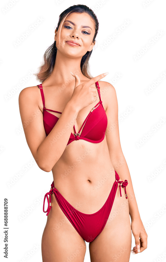 Young beautiful woman wearing bikini cheerful with a smile on face pointing with hand and finger up to the side with happy and natural expression Young beautiful woman wearing bikini cheerful with a smile on face pointing with hand and finger up to the side with happy and natural expression