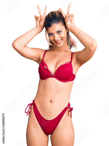 Young beautiful woman wearing bikini posing funny and crazy with fingers on head as bunny ears, smiling cheerful © Krakenimages.com