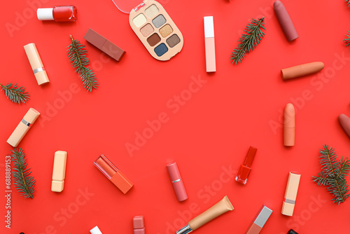 Different decorative cosmetics and Christmas tree branches on red background