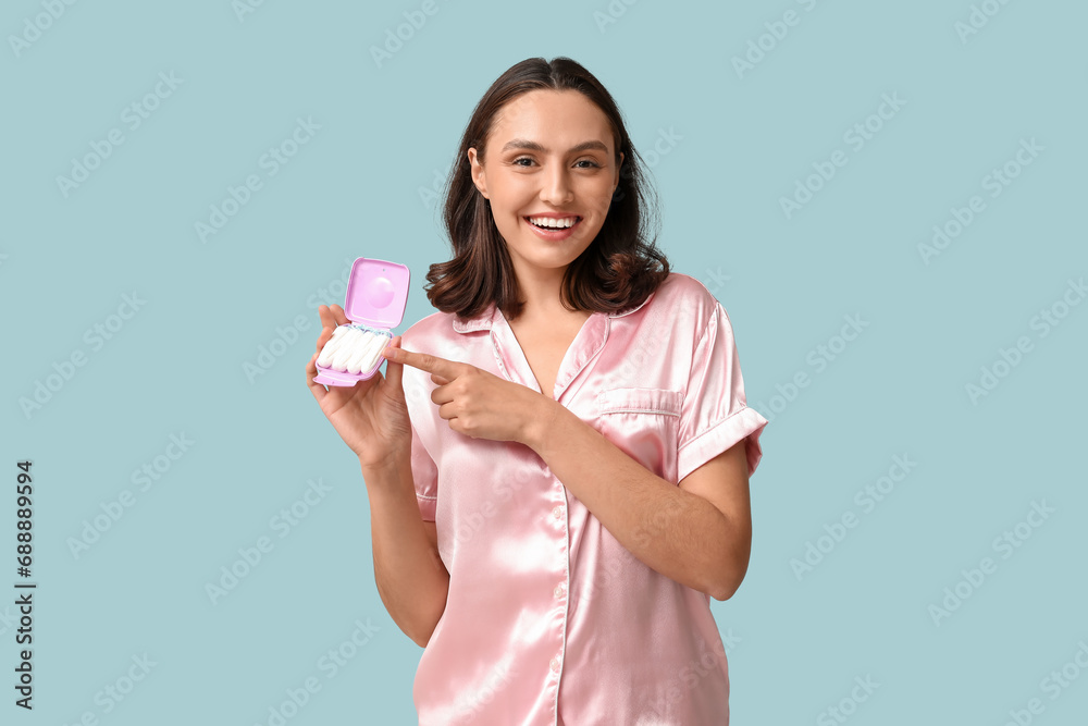 Beautiful young woman pointing at tampons storage box on blue background Beautiful young woman pointing at tampons storage box on blue background